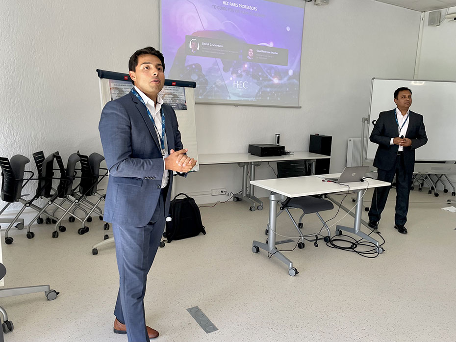 Two professors, Amariles and Srivastava, are giving a presentation on AI in a room with a large screen and chairs