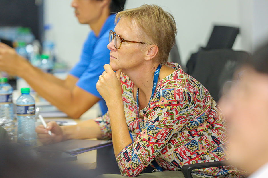 Woman with short blonde hair and glasses, wearing a colorful printed blouse or top. Sh