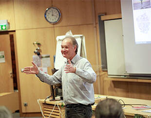 A professor passionately delivering a presentation to an engaged audience in a classroom setting