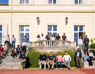 A group photo of around 30 people attending a workshop at HEC, posing on the steps of a large, elegant building with white walls and multiple windows