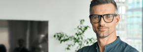 Souriant homme d'affaires mature et confiant regardant la caméra debout au bureau à la réunion d'équipe. Le directeur exécutif du chef d'entreprise masculin portant des lunettes posant pour des portraits d'entreprise est replié.